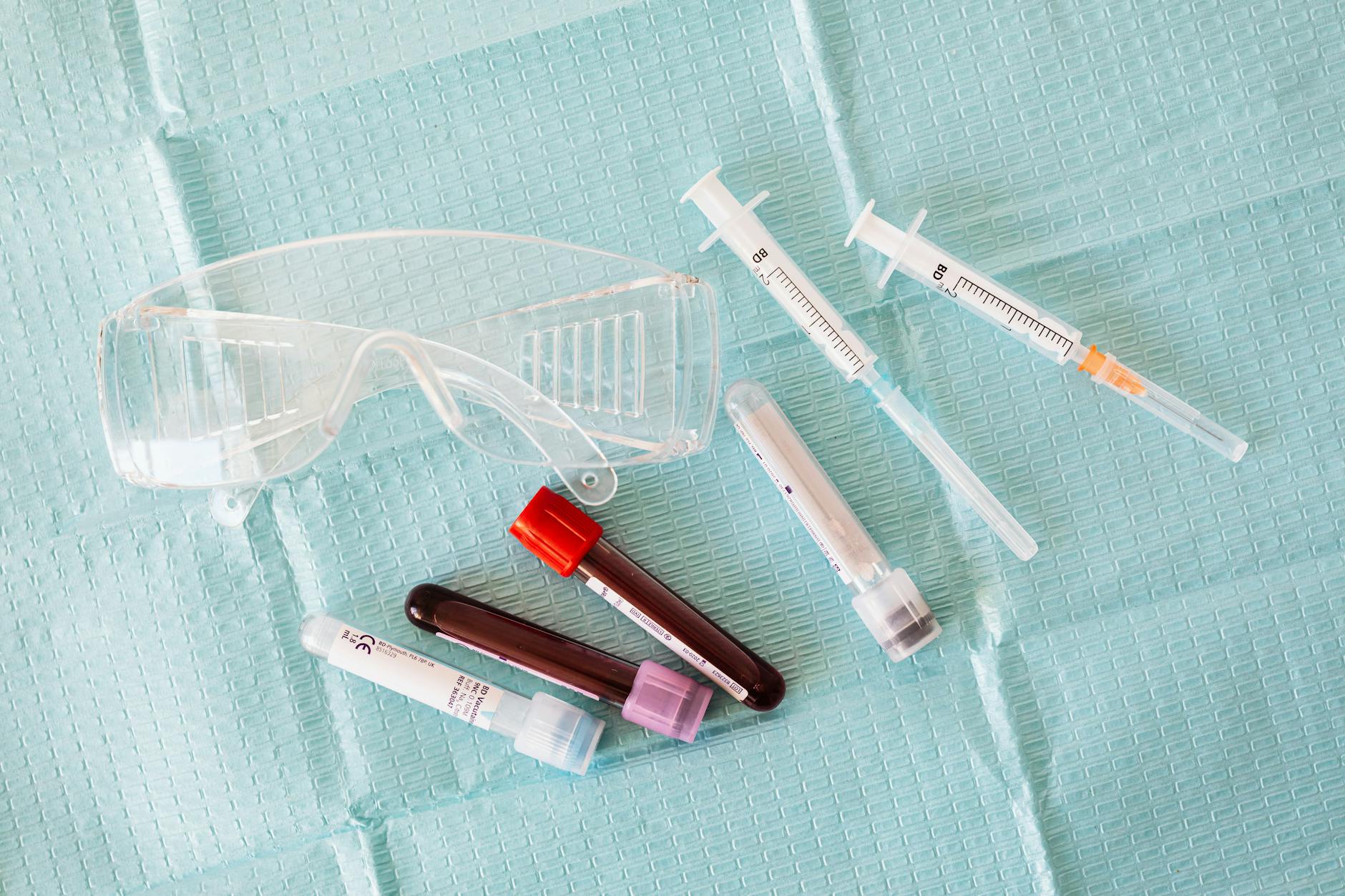 Clinical phlebotomy tray with safety glasses, fine-gauge medical syringes, and blood collection tubes on a sterile drape — illustrating the CJC-1295 + Ipamorelin GH axis evaluation