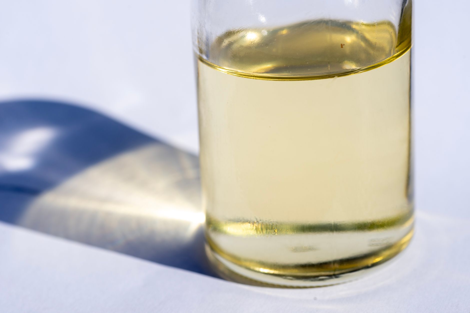 A clear, pale-yellow MCT oil in a clean glass bottle on a bright white surface, the colorless fat behind the bulletproof-coffee and keto trend