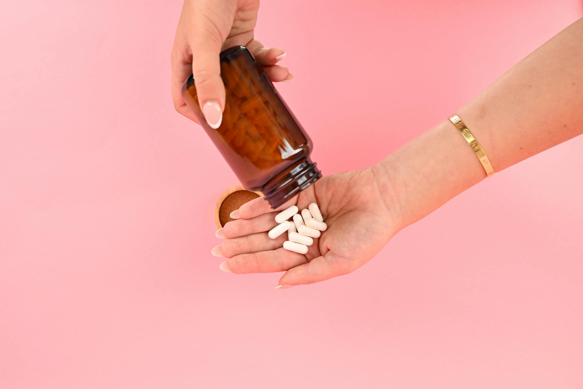 White probiotic supplement capsules pouring from an amber bottle into an open hand, gut microbiome supplements