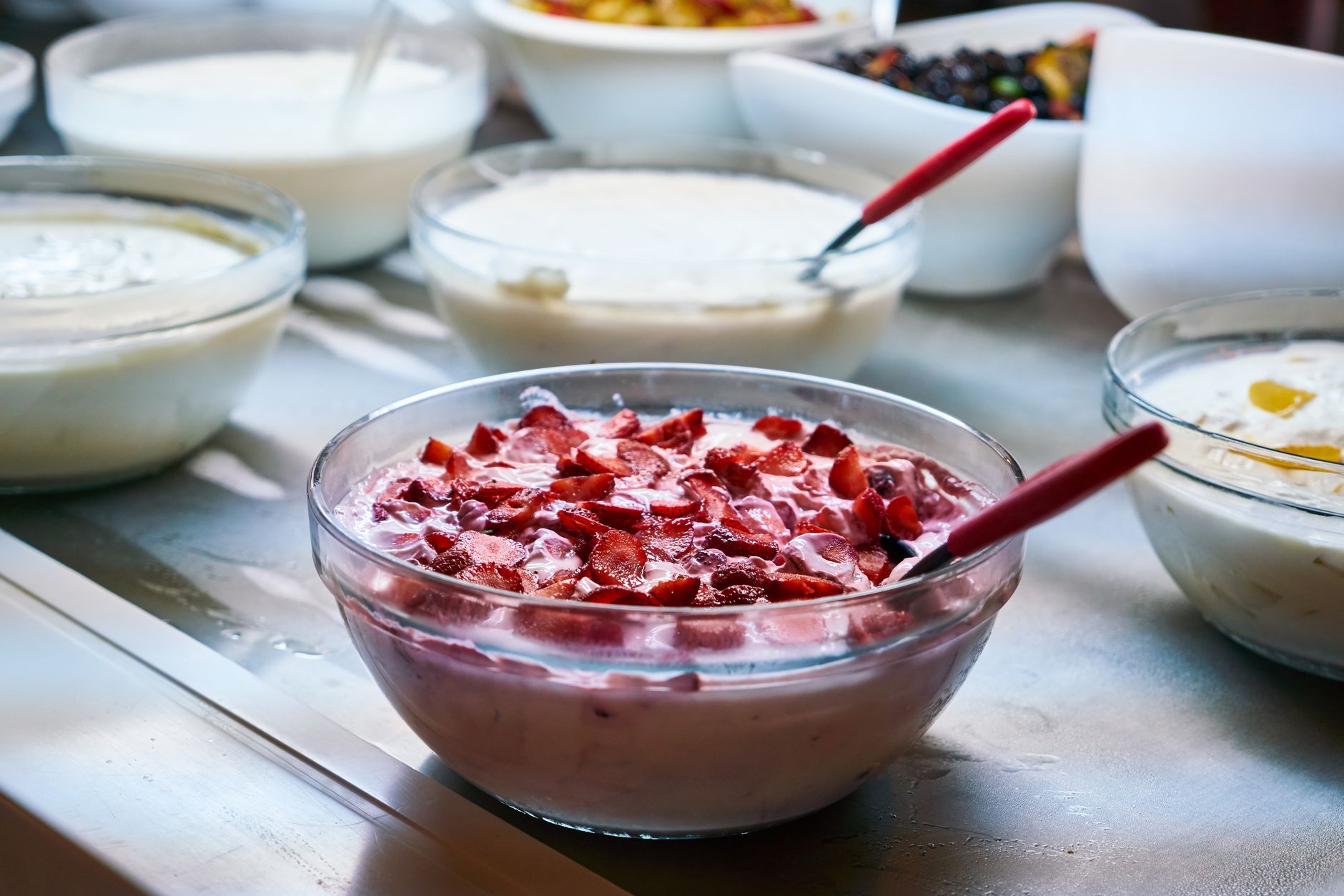 Glass bowls of yogurt and fermented dairy topped with chopped strawberries on a kitchen counter — fermented foods are a familiar source of the inactivated microbes and microbial compounds that define postbiotics