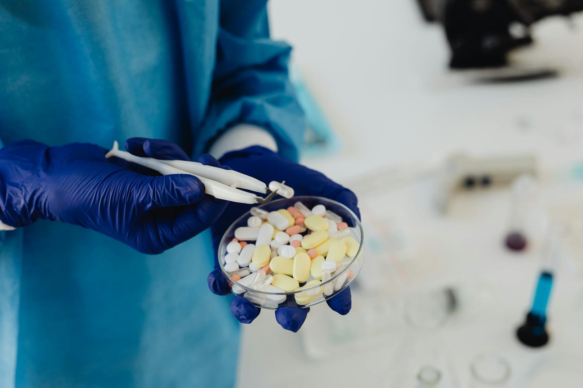 A pharmaceutical researcher in nitrile gloves using forceps to inspect assorted oral capsules in a glass petri dish &mdash; illustrating the SARMs identification and labeling problem at the center of this article